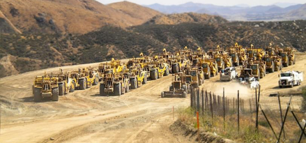 Fleet of construction equipment on sandy dune with hills in the background