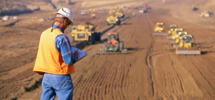 Construction worker writing on clipboard with construction equipment fleet in background