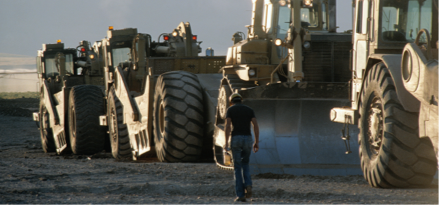 construction worker walking away from camera with four bulldozers next to him